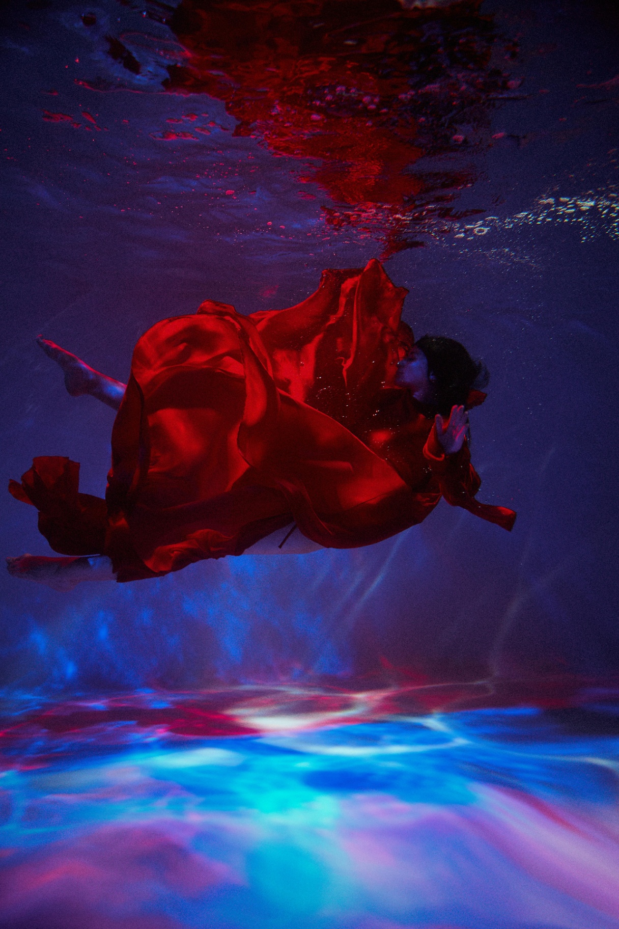 A woman in a flowing red dress floating underwater