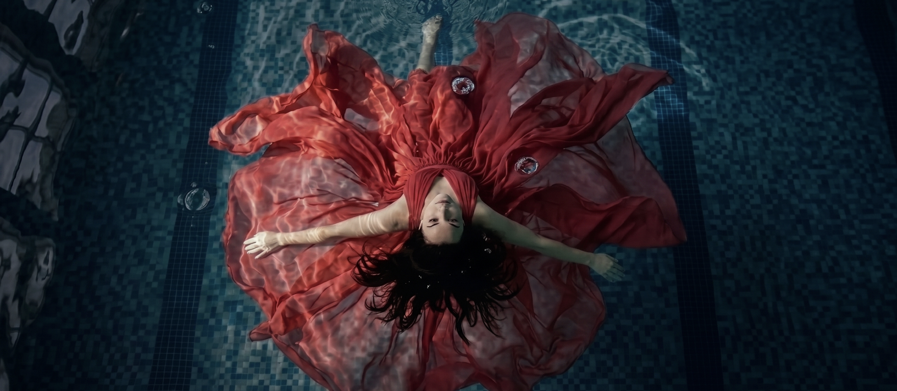 A woman in a flowing red dress floating in deep blue water